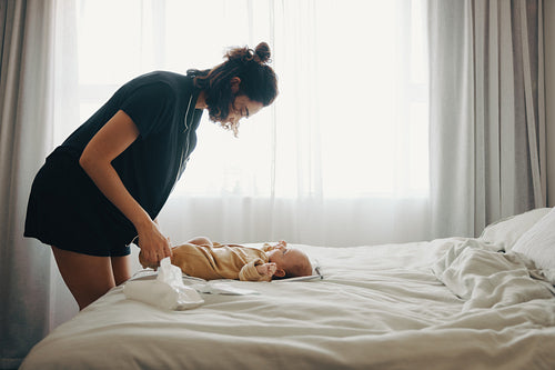 Mother changes baby on bed at home