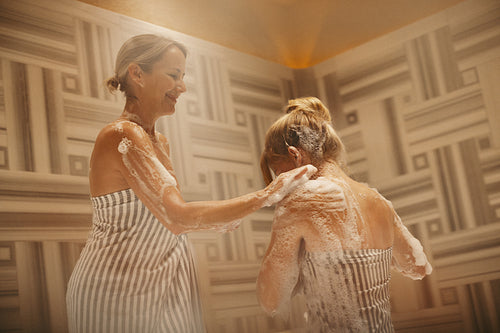 Mature woman washing younger woman with soap in a Turkish bath