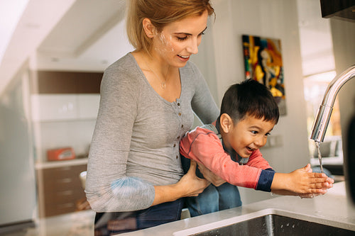 Mother helping son to wash hands after baking