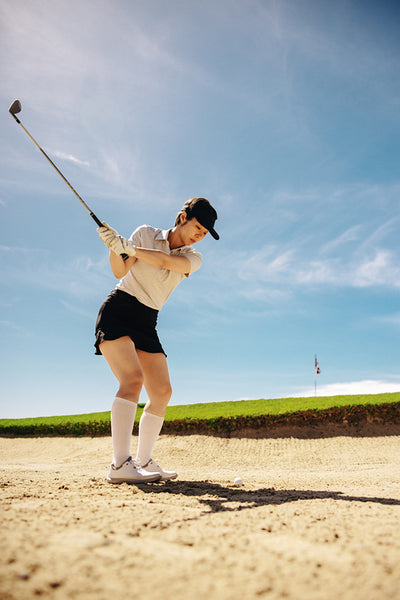 Asian female golfer skillfully aiming for a bunker escape