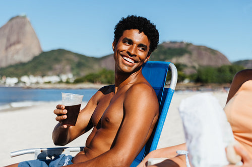 Smiling man relaxing at Praia do Flamengo beach drinking mate