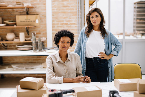 Two online store owners looking at the camera in a warehouse
