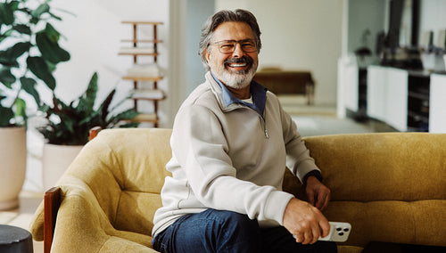 Senior man uses a smartphone while relaxing at home