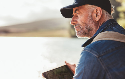 Mature man wearing cap sitting at a lake and looking at a view