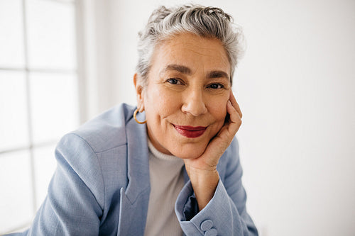 Proud business woman with grey hair sitting in her office dressed in a professional suit