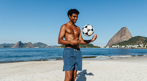 Man playing soccer on Praia do Flamengo beach with Sugarloaf Mountain in the background