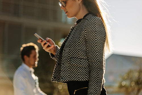 Businesswoman using mobile phone while walking on street to office