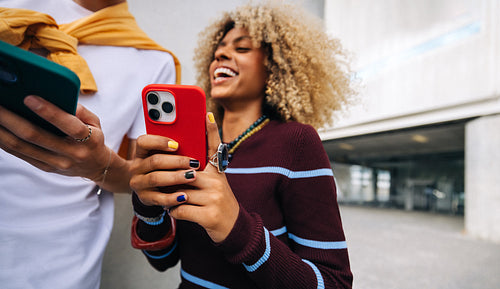 Happy friends with smartphone laughing outdoors
