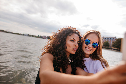 Beautiful girls taking selfie with mobile phone by the lake.