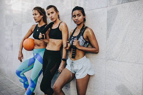 Fitness women standing outdoors after workout carrying basketball and skipping rope.
