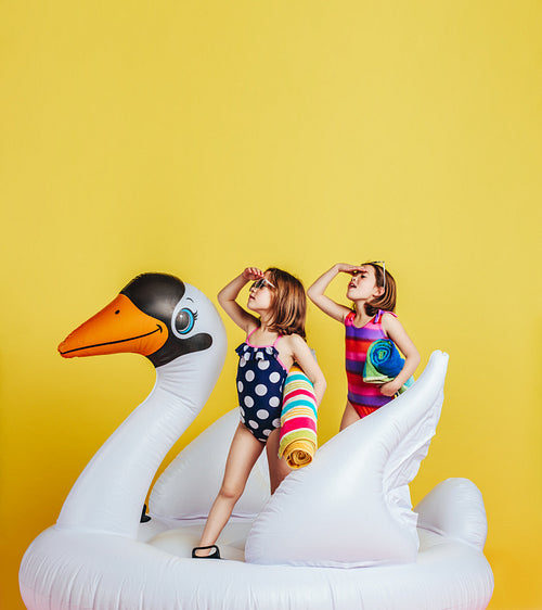 Twin girls on inflatable flamingo looking at distance