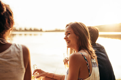 Smiling young girl sitting by a lake with friends