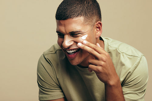 Young man using moisturizing facial cream on his flawless skin