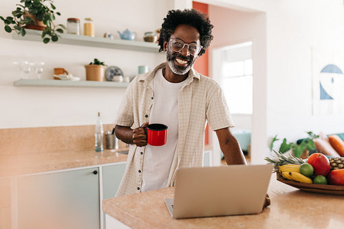 Happy Brazilian man holding a cup of café coado in his kitchen at home