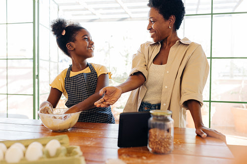 Happy mom and daughter baking bread together at the kitchen table