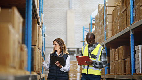 Two distribution professionals having a discussion as they do an inventory count using a tablet and a warehouse management system