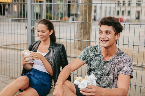 Young man and woman sitting outdoors and smiling.