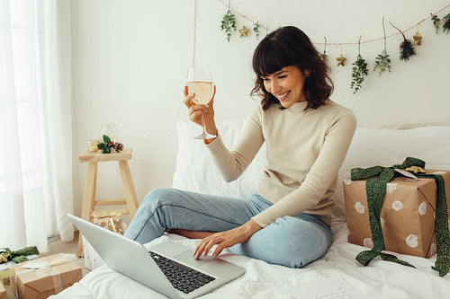 Woman celebrating christmas on video call raising wine glass