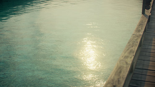 Golden sunlight sparkling on tranquil turquoise water beside a rustic wooden pier