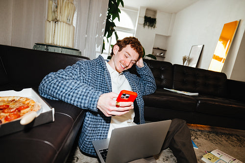 A sofa workspace frames the man as he works from home with a laptop and smartphone.