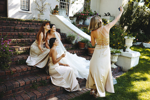 Bridesmaid taking selfie with bride and others on stone staircase outdoors