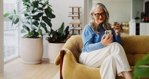 Senior woman uses a smartphone while relaxing at home