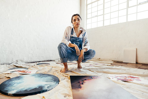 Female painter squatting in the middle of her paintings