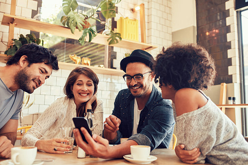 Friends in a cafe looking at the photos on mobile phone 