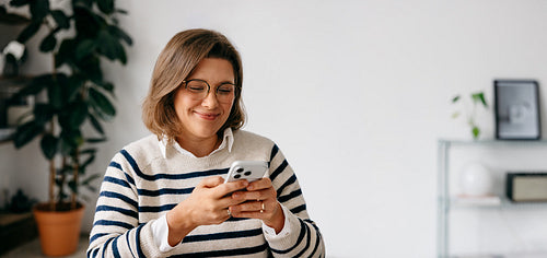 Using her smartphone for messaging, the woman manages work in a home office