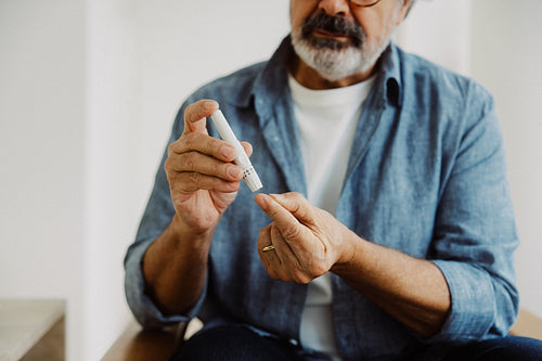 Senior man checks blood glucose with a lancet at home