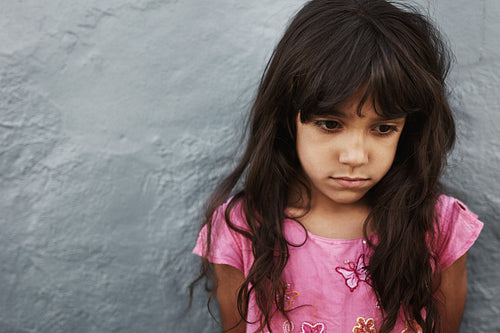Unhappy little girl standing against grey wall