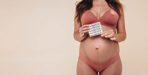 Pregnancy nutrition: Woman holding a pack of prenatal multivitamin supplements on her baby bump