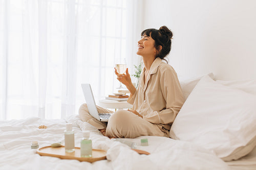Woman doing video call on laptop holding wine glass