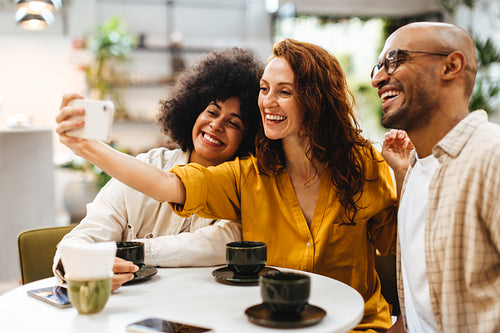 Three friends in a cafe taking a selfie on a smartphone