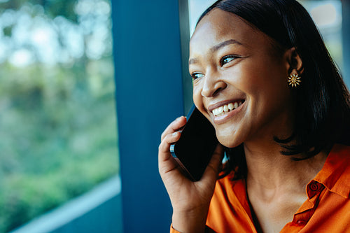 Cheerful woman enjoying a phone call by the window