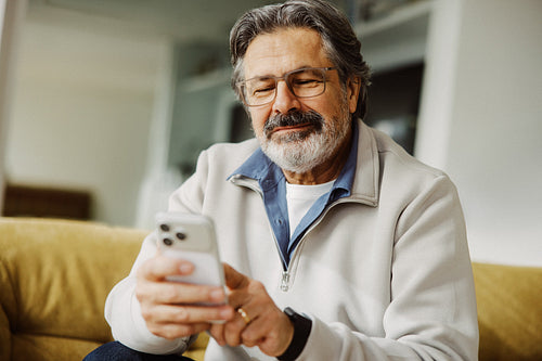 Senior man uses a smartphone while relaxing at home
