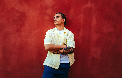 Latin man stands with crossed arms against a red wall in an urban outdoor portrait