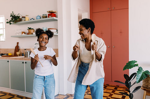 Joyful mother and daughter singing and dancing at home