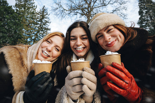 Women hold warm drinks with friends in the snow