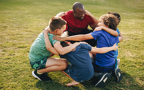 Coach and school kids huddling in a sports ground