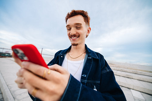 Smiling man using phone outdoors by the waterfront