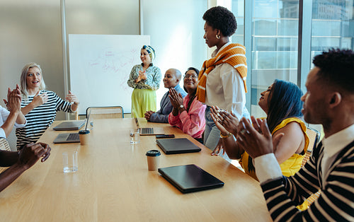 Successful board meeting with diverse team applauding presentation in modern office setting