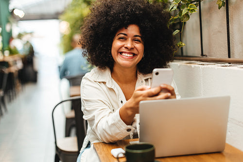 Cheerful young woman using a mobile phone and laptop to work in a coffee shop