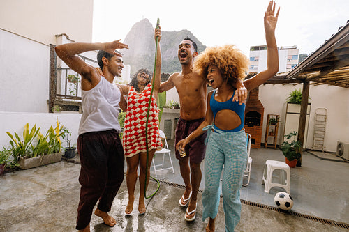 Group of friends splashing each other with a garden hose in Rio