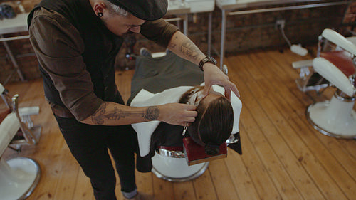 Barber styling beard with razor at barbershop