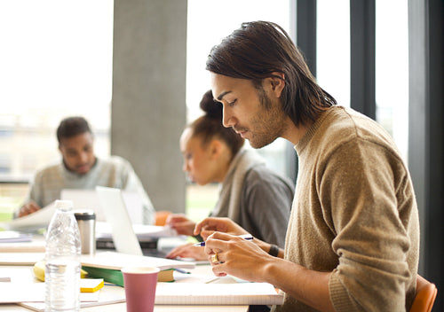 Young man talking notes for study in college library