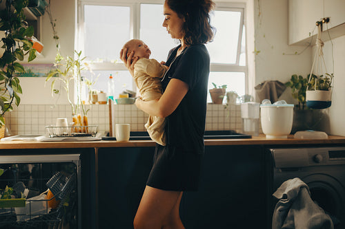 Mother holds baby in bright kitchen at home