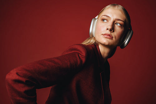 Headphones frame the woman in a red studio portrait with fashion styling