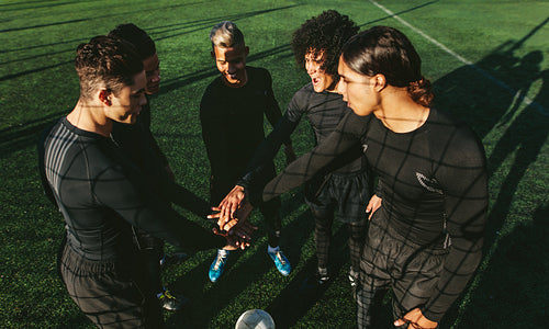 Soccer team stacking hands at football field
