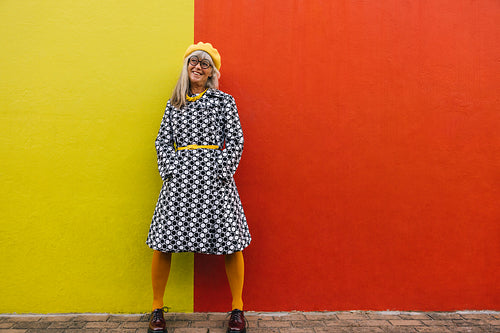 Cheerful senior woman looking away thoughtfully against a colour
